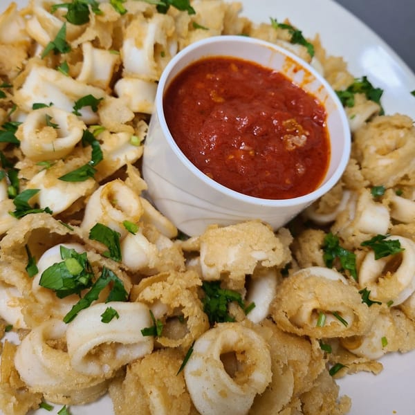 Crispy fried calamari rings with fresh parsley, served with a side of red marinara sauce.