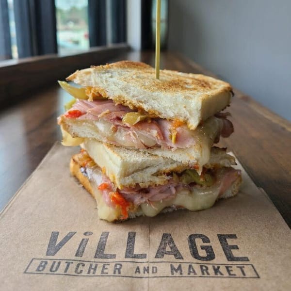Stacked grilled sandwich with melted cheese, ham, and peppers on Village Butcher and Market paper.