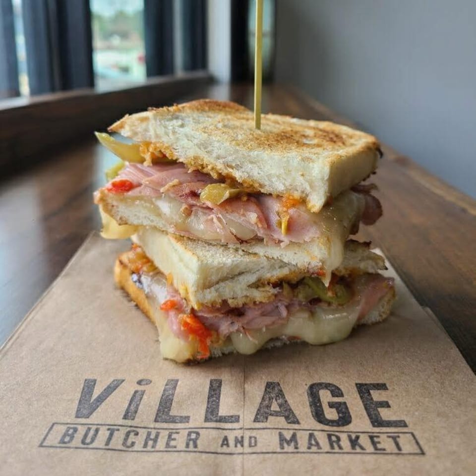 Stacked grilled sandwich with melted cheese, ham, and peppers on Village Butcher and Market paper.