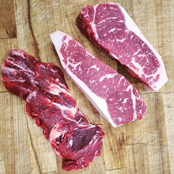 Three cuts of raw beef, two steaks and one irregular cut, on a wooden cutting board.