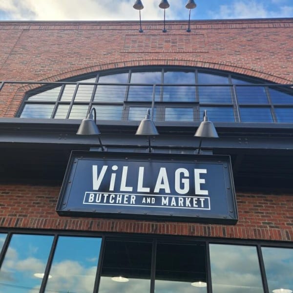 Exterior of Village Butcher and Market, a brick building with a large arched window and prominent sign.