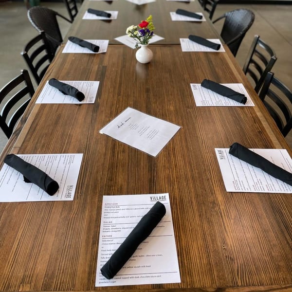 A long wooden table set with menus, black napkins, and a small vase of flowers.