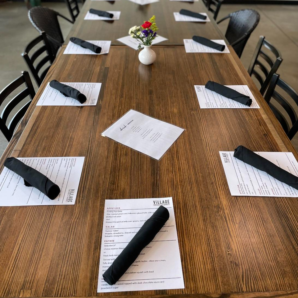 A long wooden table set with menus, black napkins, and a small vase of flowers.