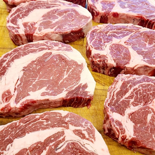 Several raw, marbled steaks with white fat and red meat on a yellow cutting board.