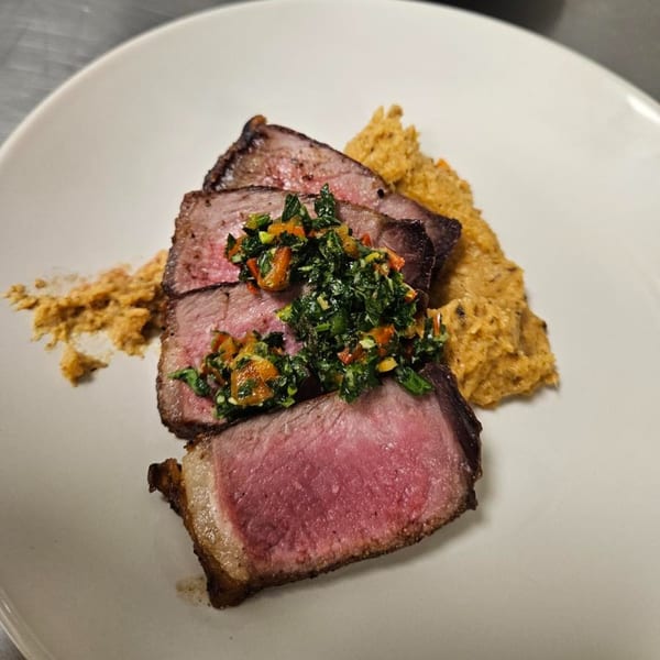 Three slices of medium-rare steak topped with chimichurri and a side of mashed sweet potatoes.