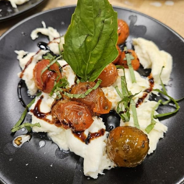Caprese salad with roasted tomatoes, fresh mozzarella, basil, and balsamic glaze on a black plate.