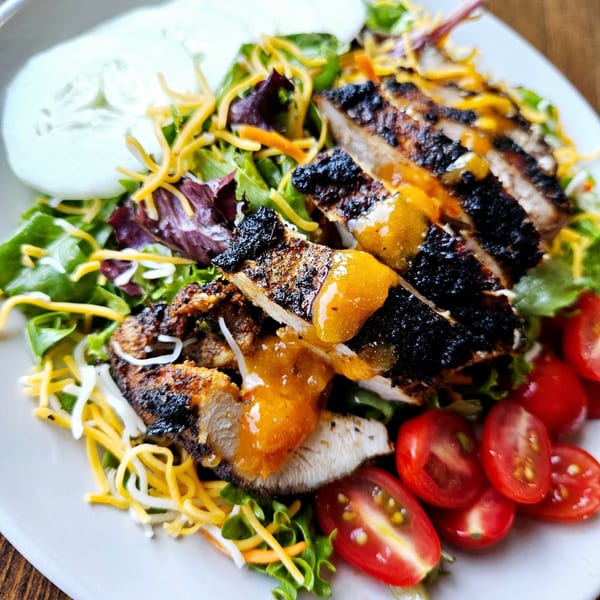 Grilled chicken salad with mixed greens, shredded cheese, cherry tomatoes, and cucumber slices.