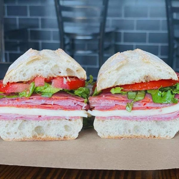 Two Village Butcher and Market sandwiches, filled with deli meats, cheese, lettuce, and tomatoes on ciabatta bread.